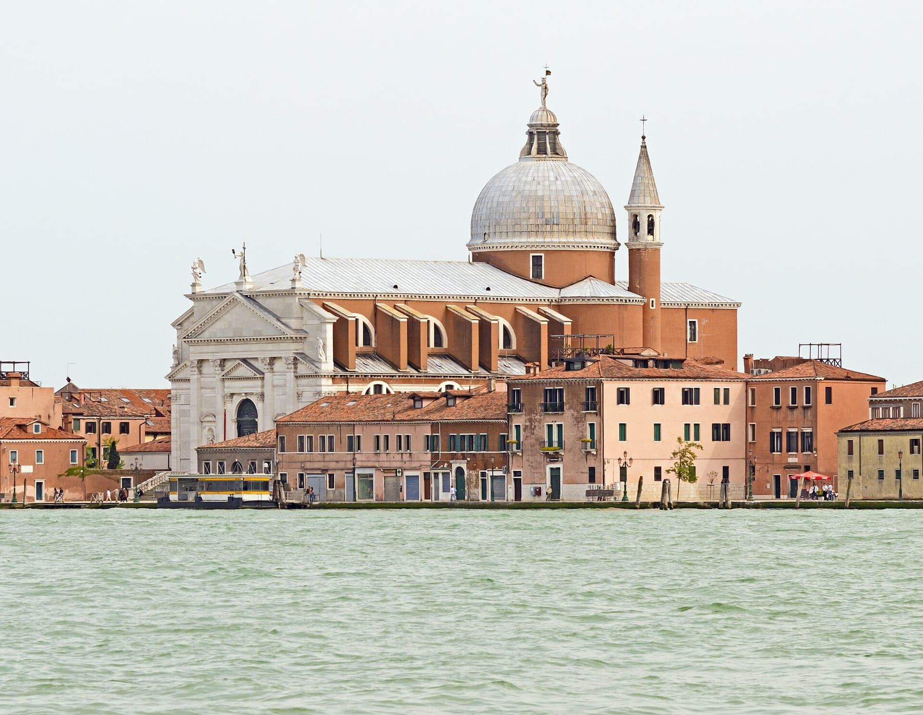 La Giudecca vista dal canale: la chiesa del Redentore con la facciata bianca e la cupola, tra case color mattone lungo la fondamenta